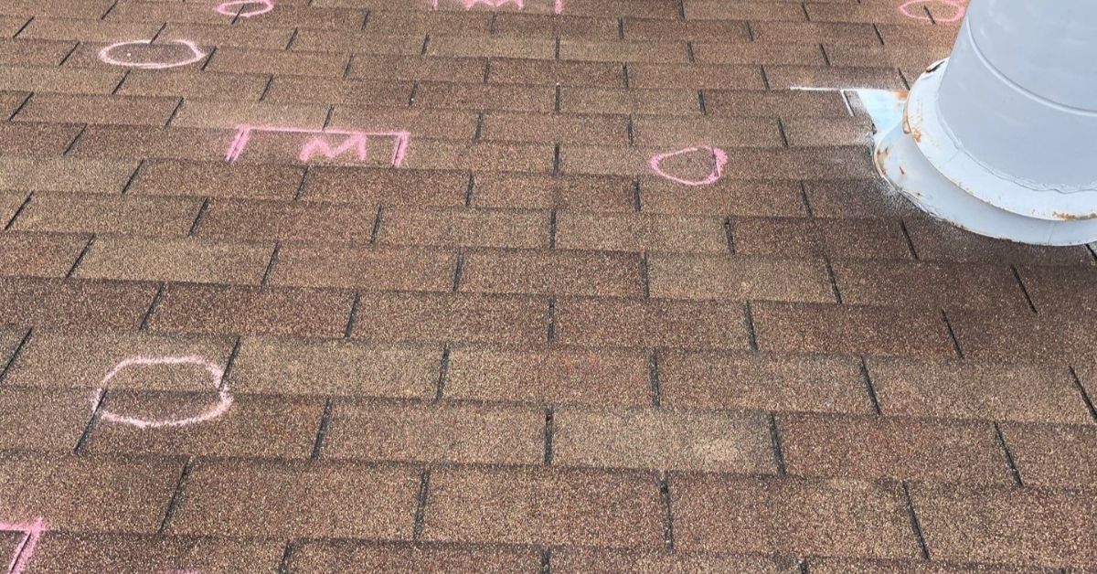 Asphalt shingle roof with chalk markings highlighting suspected hail impact points and areas of granule loss during a professional inspection